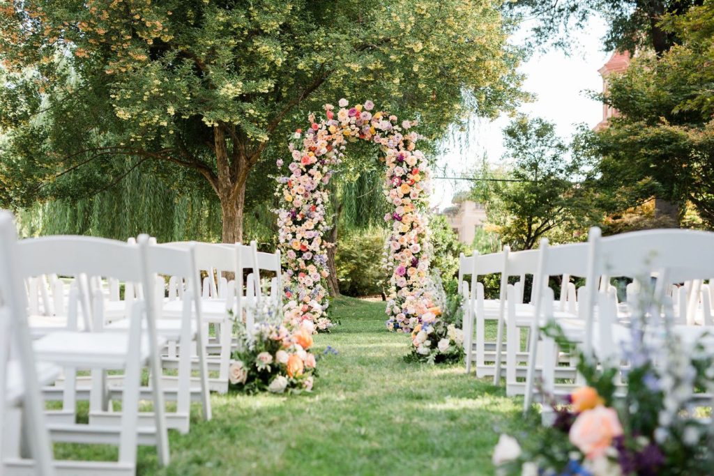 Backyard Wedding Inspo: Outdoor Ceremony Space with White Garden Chairs and Floral Arches